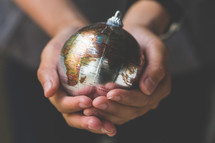 cupped hands holding a globe ornament 