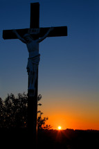 sculpture of crucifixion of Christ in front of a sunset