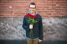 Looking for love -- a man standing by a brick building with a bouquet of roses in his hand.