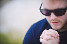 a man in sunglasses with praying hands 