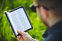 a man reading a Bible in grass
