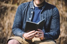 a man reading a Bible sitting on rocks 