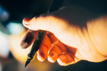 A hand with ink smudges holding an ink pen.