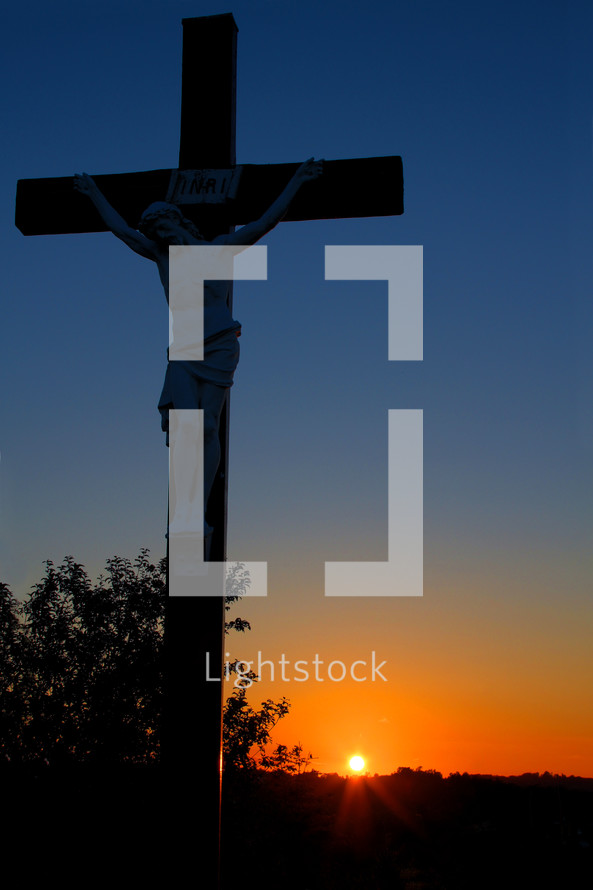 sculpture of crucifixion of Christ in front of a sunset