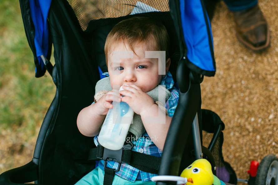 infant boy drinking a bottle in a stroller 