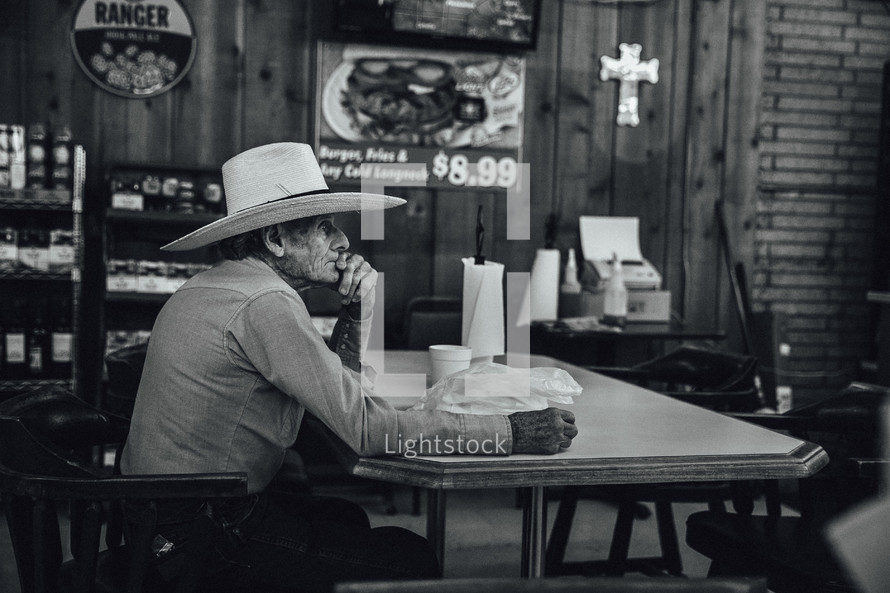 elderly man in a cowboy hat sitting in a restaurant 