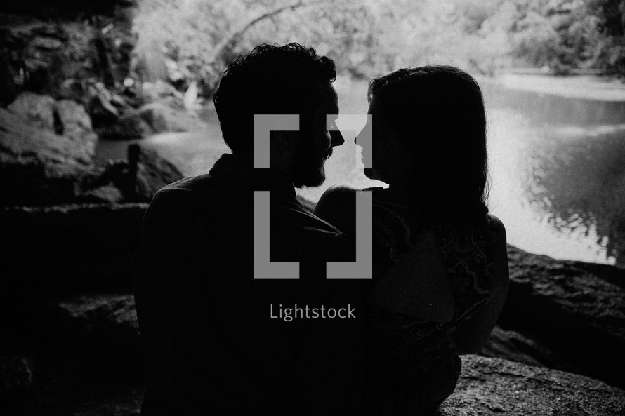 Silhouette of an embraced couple sitting in a cave by a lake.