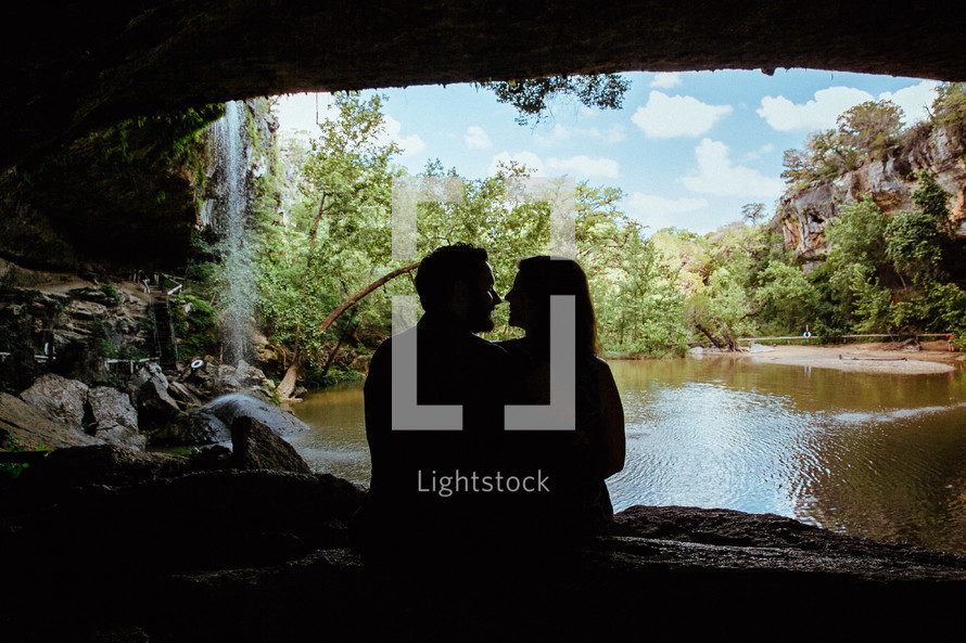 Silhouette of an embraced couple sitting in a cave by a lake.