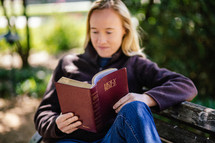 woman sitting on a park bench reading a Bible