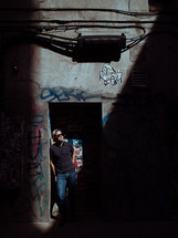 man standing in a doorway of a graffiti covered building 