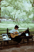 man sitting in a park playing a guitar for money 
