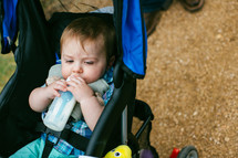 Infant drinking from a bottle while riding in a stroller.