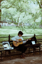 man playing a guitar for money in a city park 