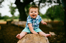 infant boy sitting on a log 