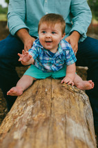Infant child sitting on a log outside.
