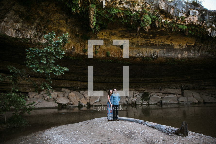 couple standing at the bottom of a cliff and cave 