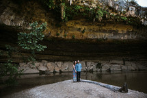 couple standing at the bottom of a cliff and cave 