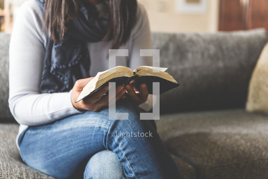 a woman sitting on a couch reading a Bible 