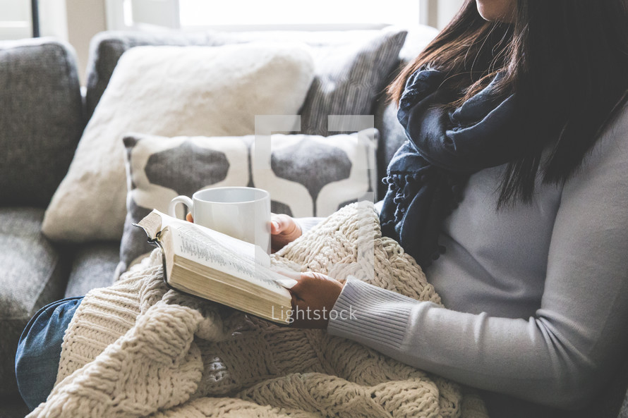 a woman reading a Bible snuggled in a blanket 