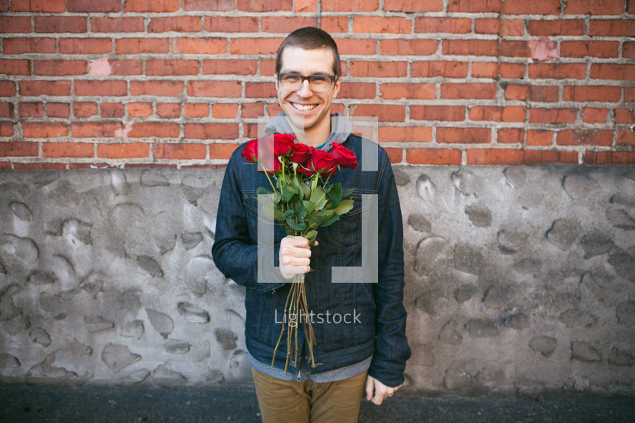 Looking for love -- a man standing by a brick building with a bouquet of roses in his hand.