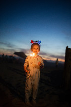 a little girl in pajamas on a beach holding a sparkler 