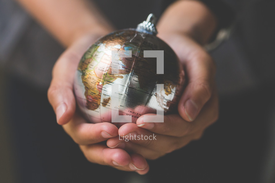 cupped hands holding a globe ornament 