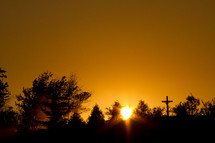 sun setting behind the trees and a silhouette of a cross