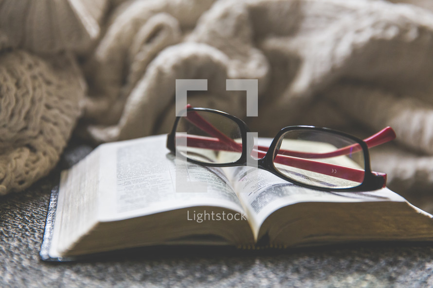 reading glasses, open Bible, and blanket on a couch 