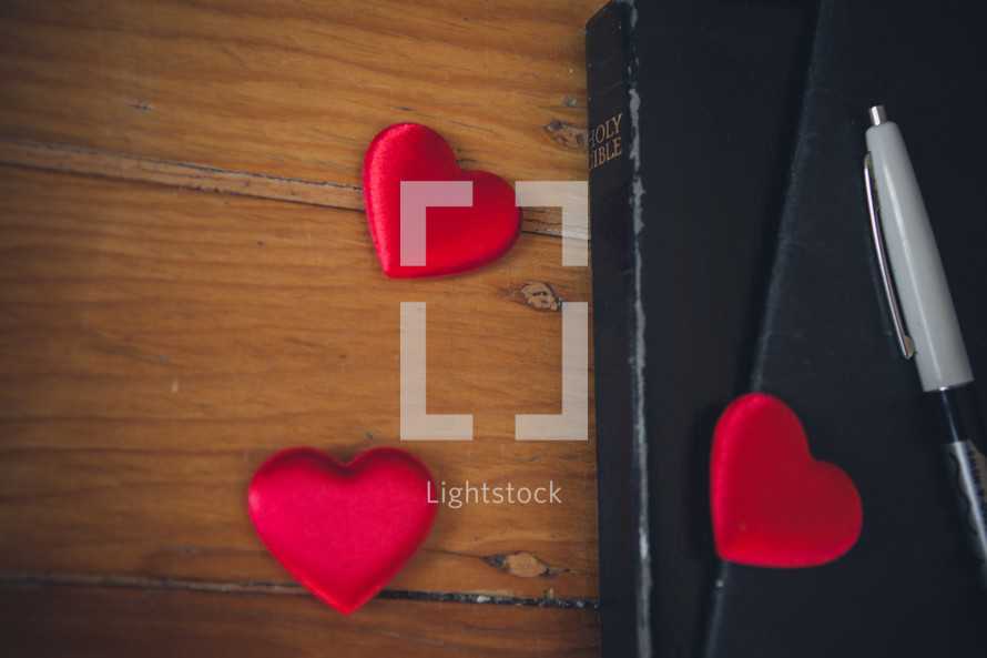 Red hearts on a wooden table with a Bible, journal and pen.