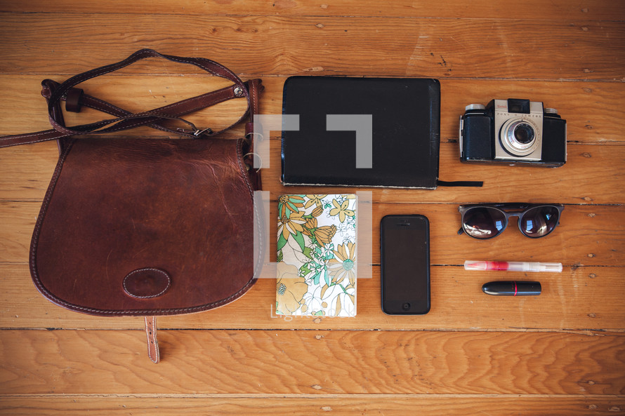 Contents of a purse - journal, cellphone, sunglasses, pen, lip stick, Bible, camera