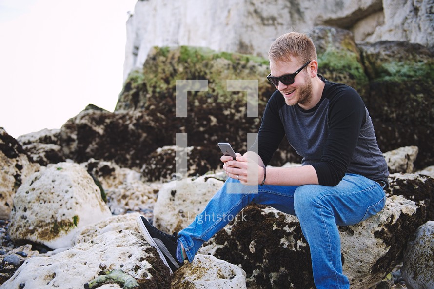 a man sitting on rocks checking his cellphones 