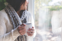 a woman holding a coffee mug and looking out a window 