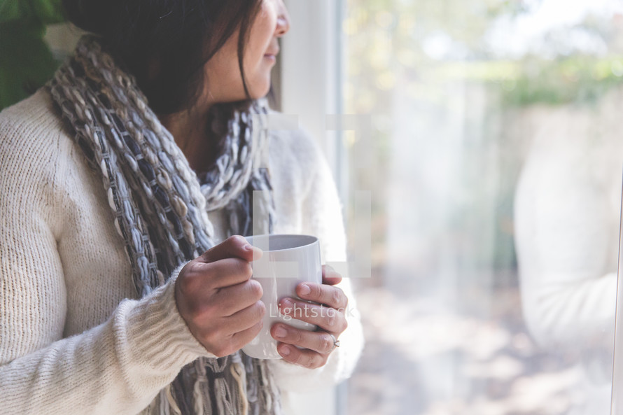 a woman holding a coffee mug and looking out a window 