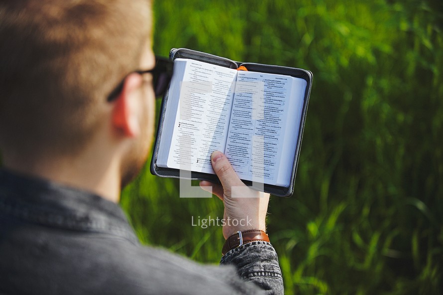 a man reading a Bible in grass 