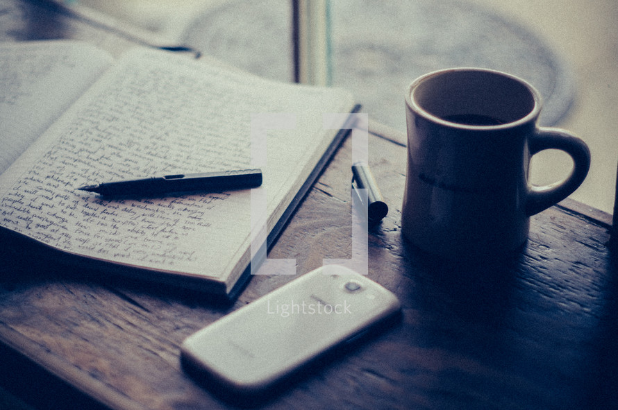 pen on a journal, cellphone, and coffee mug in a window sill 