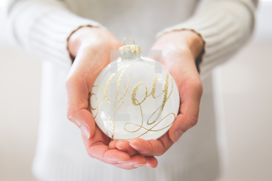 a woman holding an ornament with the word Joy on it 