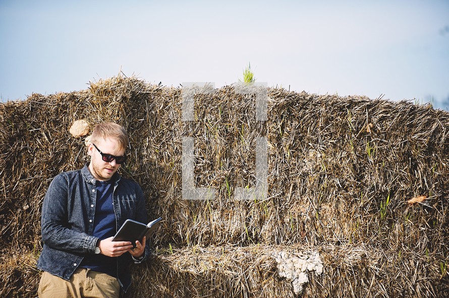 a man reading a Bible on a hay bale 