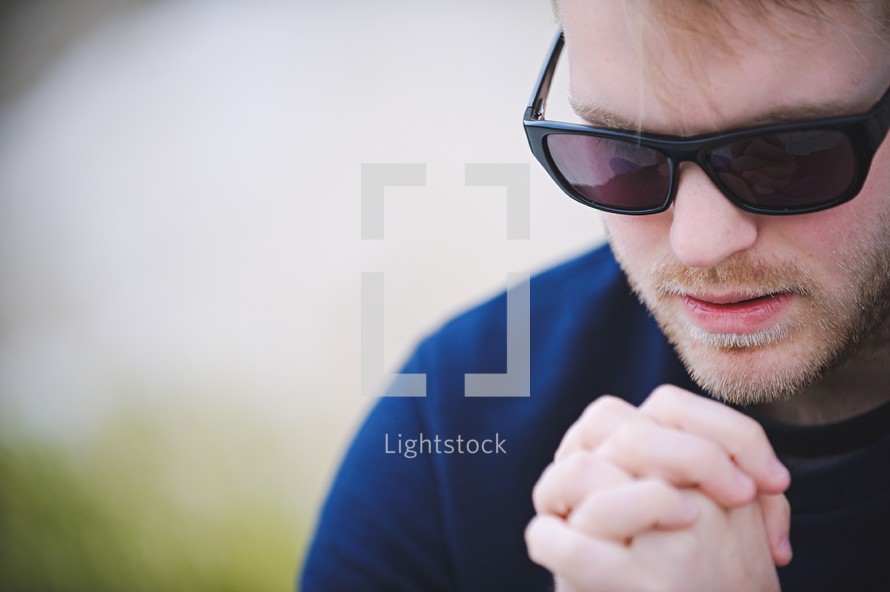 a man in sunglasses with praying hands 