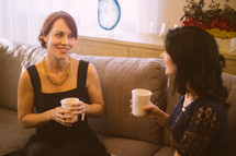 Two women talking together on a couch, with coffee.