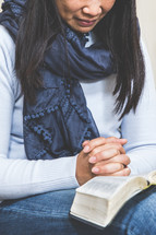 a woman praying over a Bible in her lap 