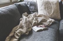reading glasses, blanket, and open Bible on a couch 