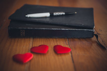 A Bible a pen and red candy hearts. 