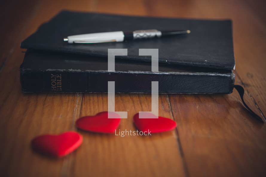A Bible a pen and red candy hearts. 