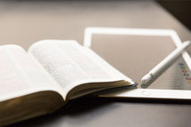 An open Bible, an electronic tablet, and a stylus.