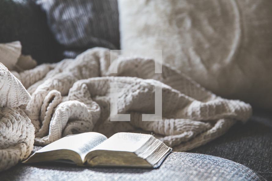 open Bible and blanket on a couch 