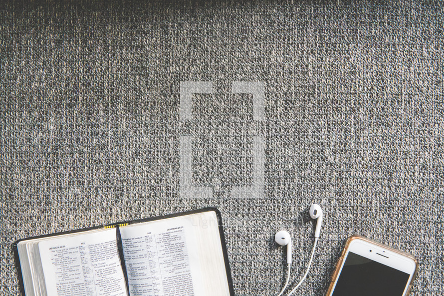 cellphone, earbuds, and open Bible on a couch 