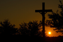 sun setting behind a sculpture of the crucifixion of Christ