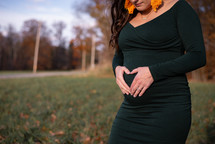 Woman wearing a green, maternity dress with hands forming a heart over the baby