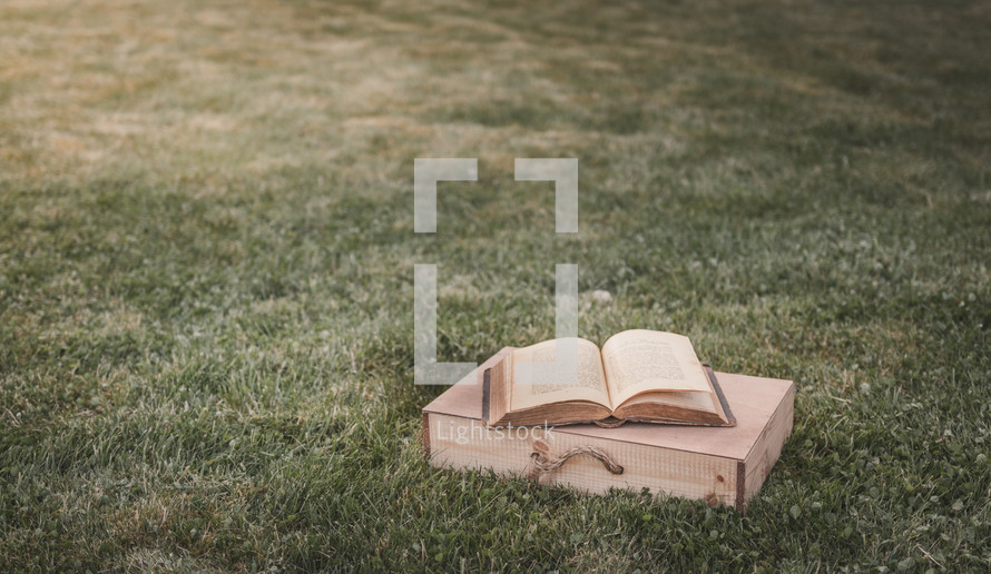 open Bible and wood box in grass 