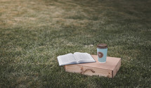 coffee cup with cross on grass with Bible and wood box 